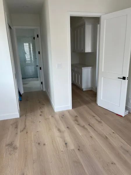 Hardwood flooring in a room with white doors and a hallway leading to a bathroom.