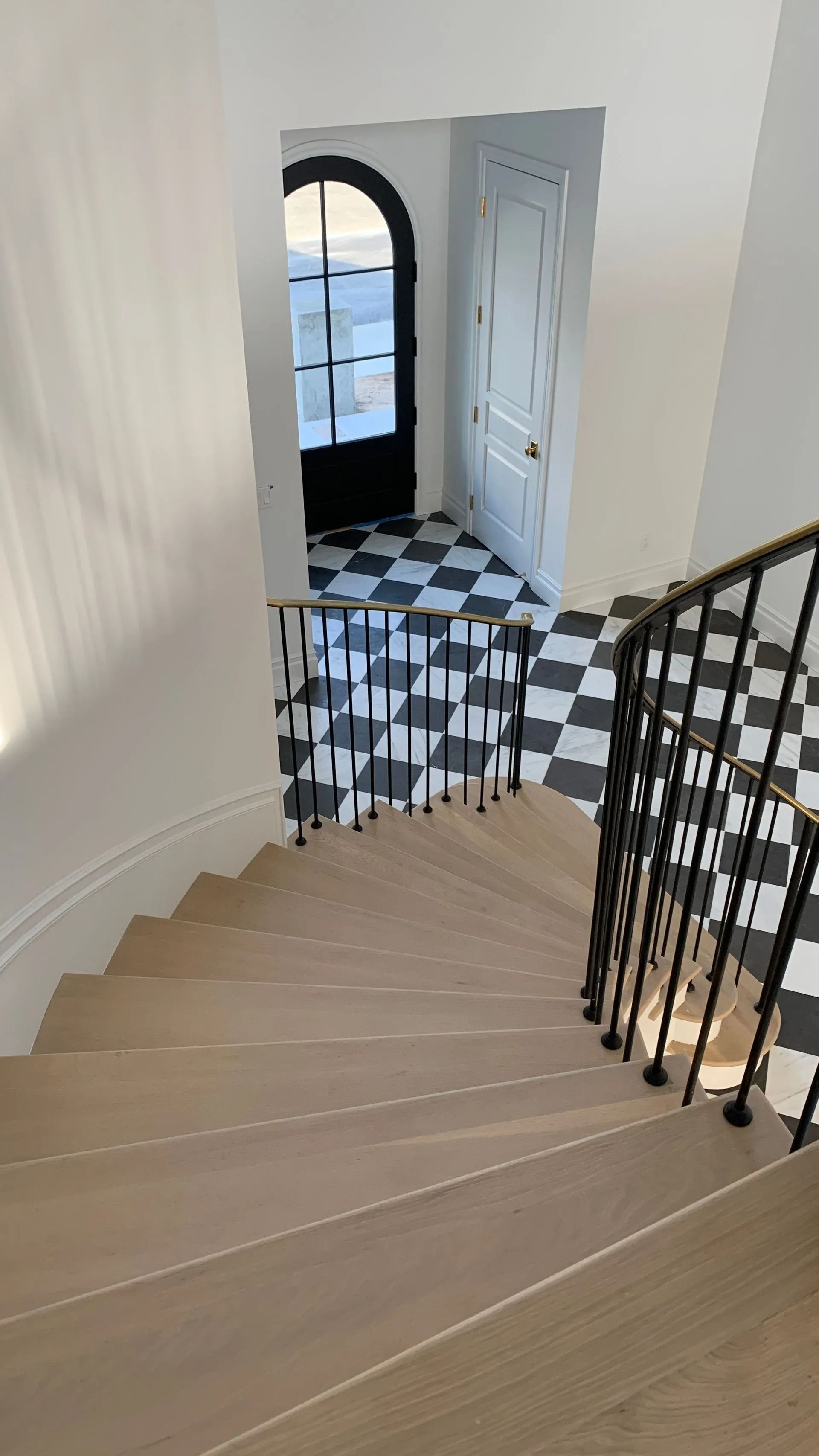 Wooden staircase with black metal railing, leading to a checkered floor, doorway, and white walls.