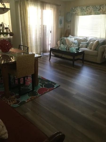 Living room with wood flooring, light-colored couch, dining table, and sliding glass door.