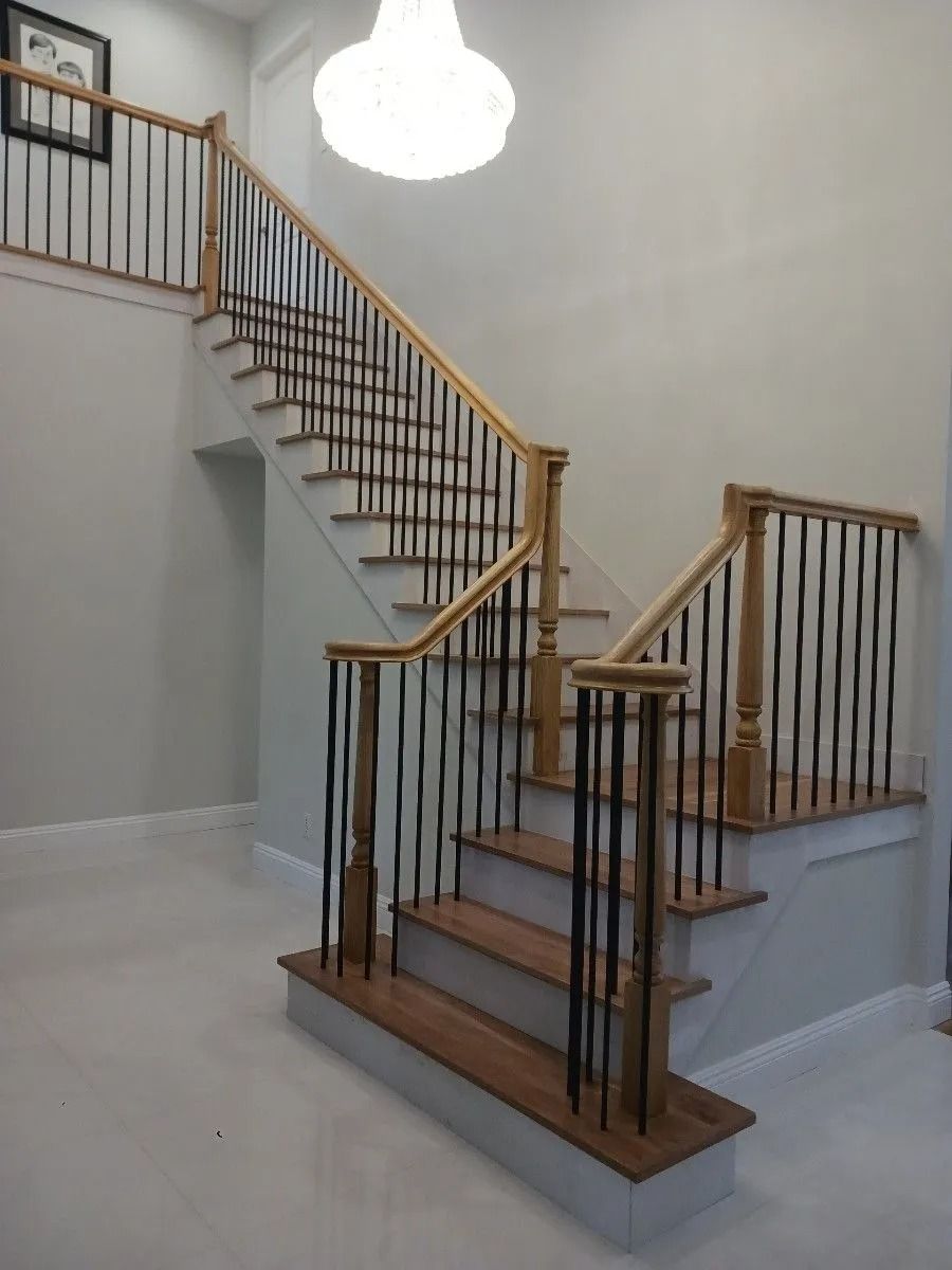 Wooden staircase with black railings, a white ceiling light, and light gray walls.