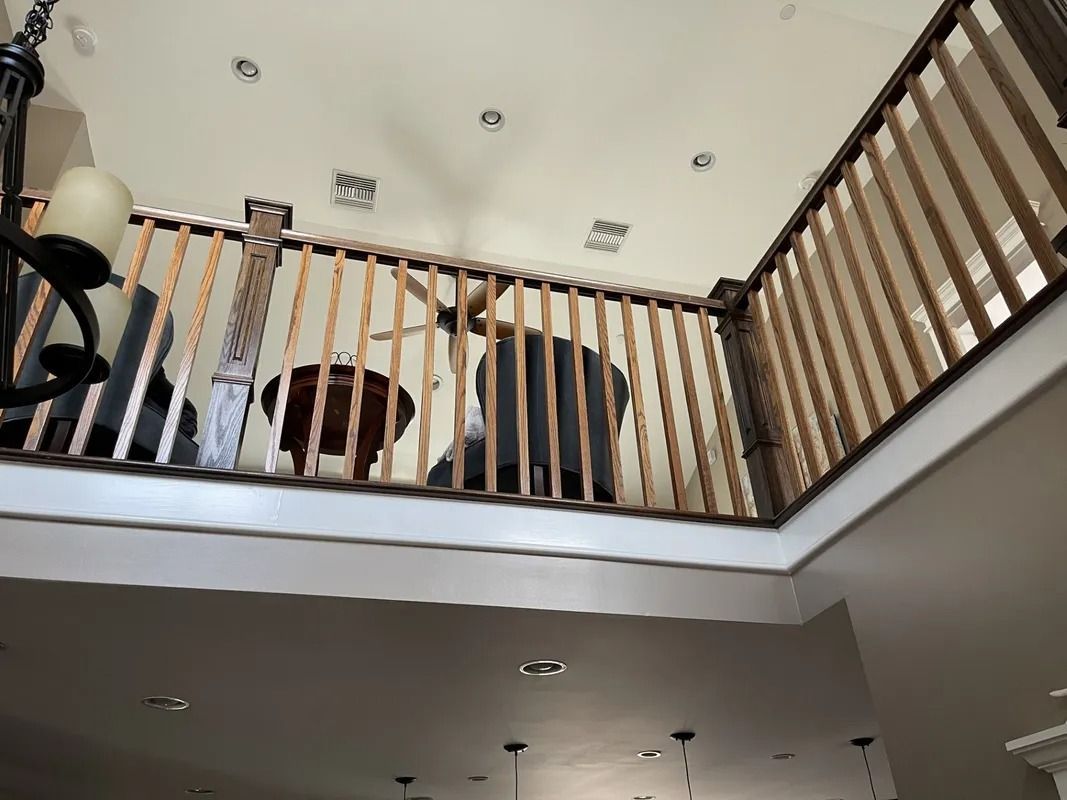 Interior view of a second-floor railing overlooking a lower level. Sunlight highlights the wood.