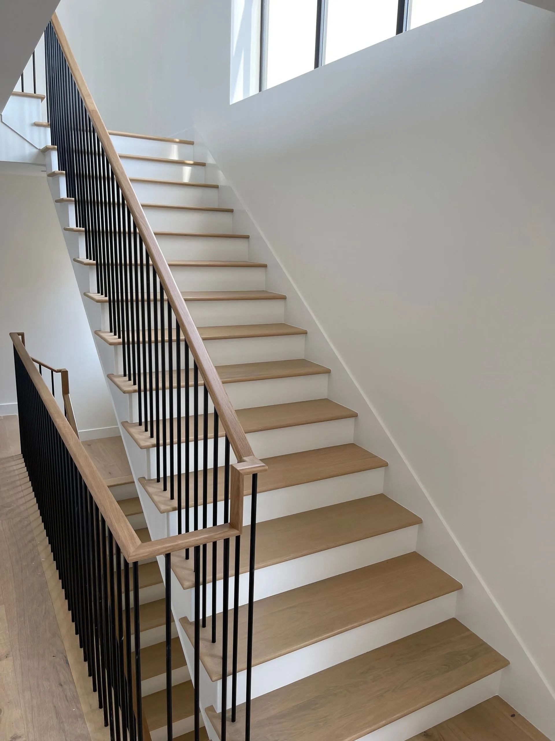 Staircase with light wood steps, white risers, black metal balusters, and a light wood handrail.