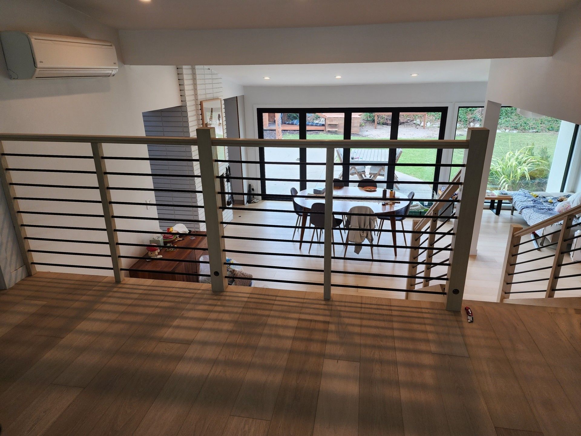 Interior view of a modern home with a staircase, railing, and open dining area visible through glass doors.