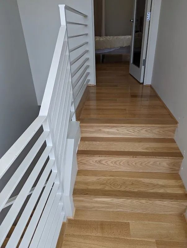Wooden stairs leading up to a hallway with light wood floors and a white railing.