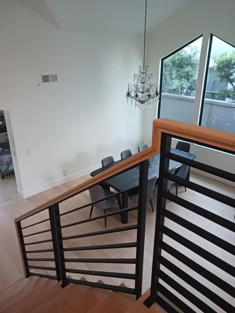 High-angle view of dining room with chandelier, table, and chairs, and a staircase with wood and black metal railing.