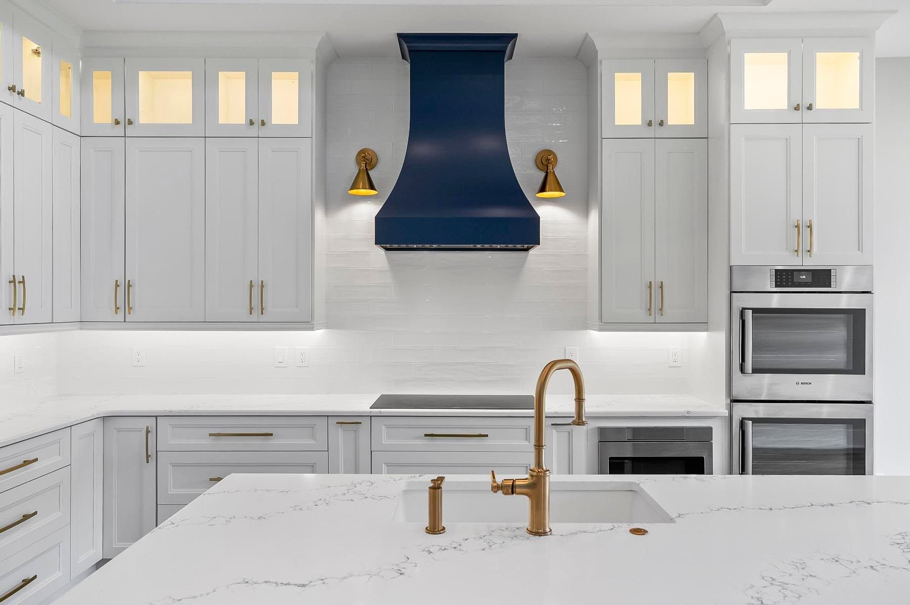 Bright white kitchen with blue range hood, brass faucet, and marble island countertop