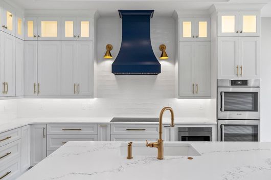 Bright white kitchen with blue range hood, brass faucet, and marble island countertop