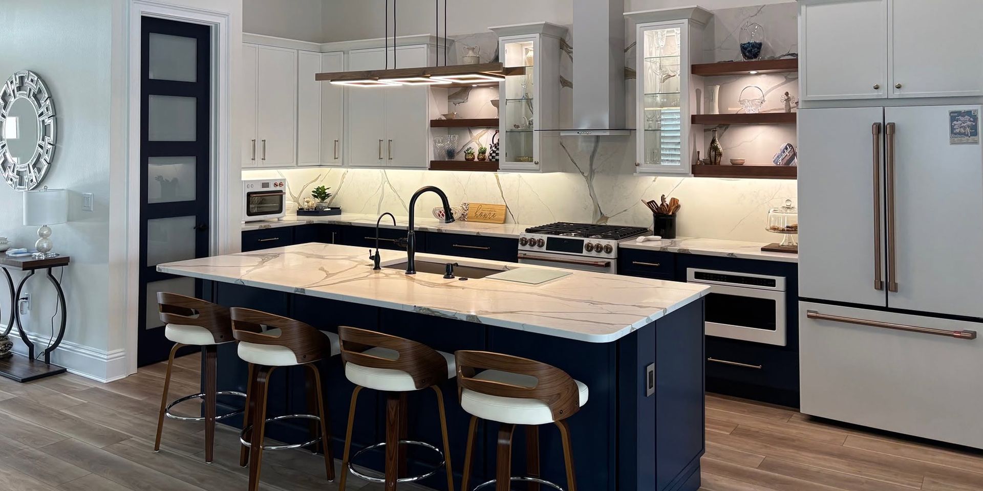 Modern kitchen with large island, white cabinets, stainless fridge, and bar stools under pendant lights
