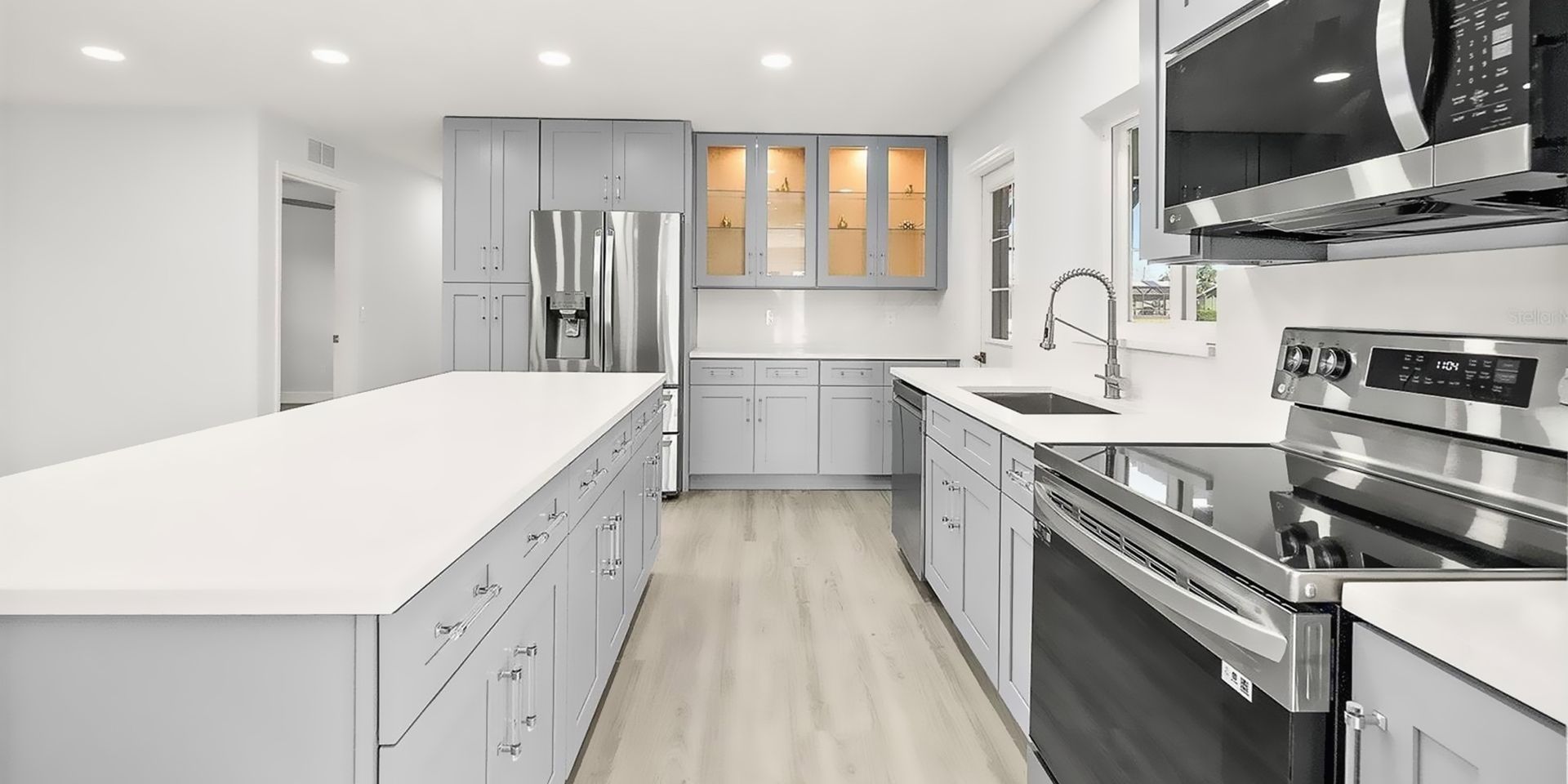 Bright modern white kitchen with island, stainless steel appliances, and light wood floors