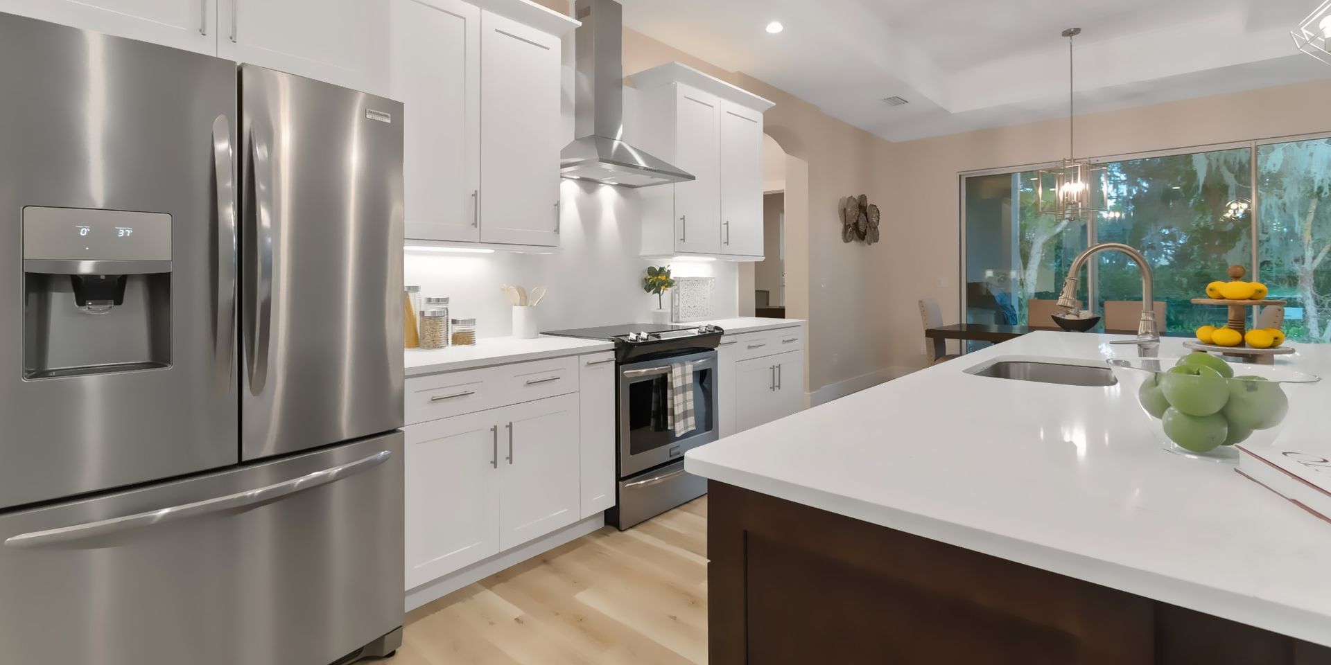 Modern white kitchen with stainless steel appliances and a large island by a window