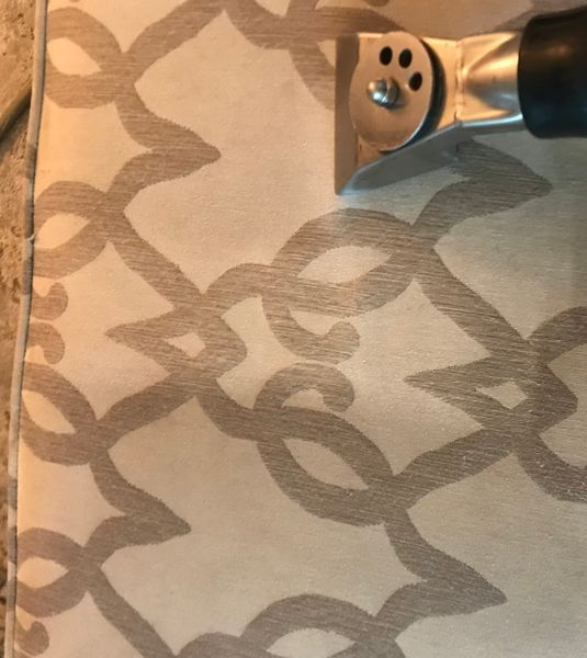 Upholstery being cleaned with a steam cleaner; light beige fabric with gray patterned design.