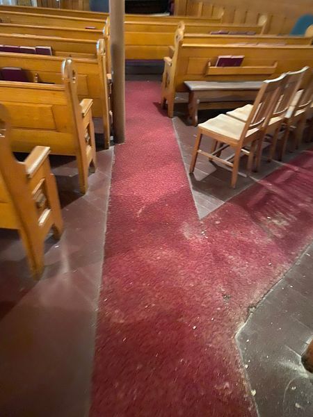 Red carpet aisle in a church, flanked by wooden pews and chairs.