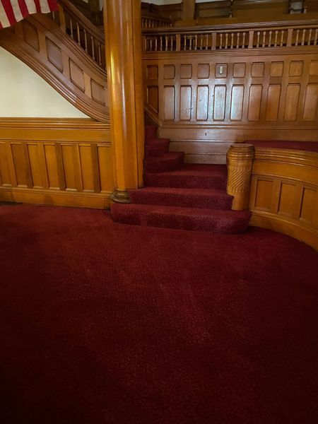 Wooden staircase with red carpet, ornate wood paneling, and a large wooden pillar.