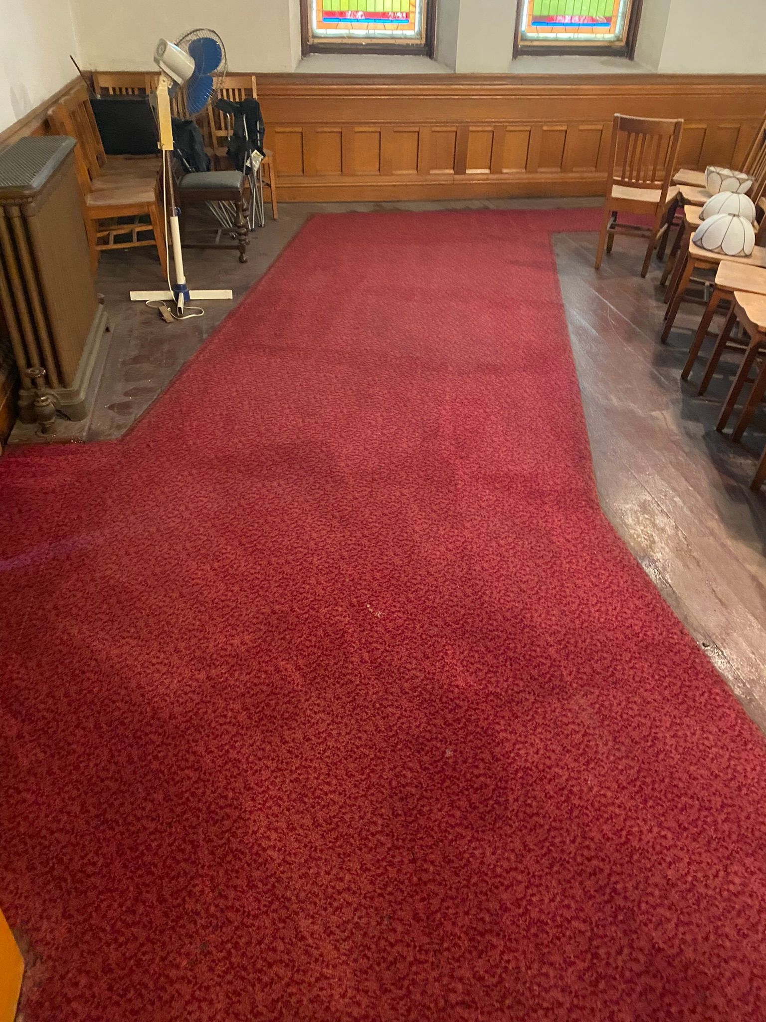 Red carpet runner in a wood-paneled room with chairs and stained-glass windows.