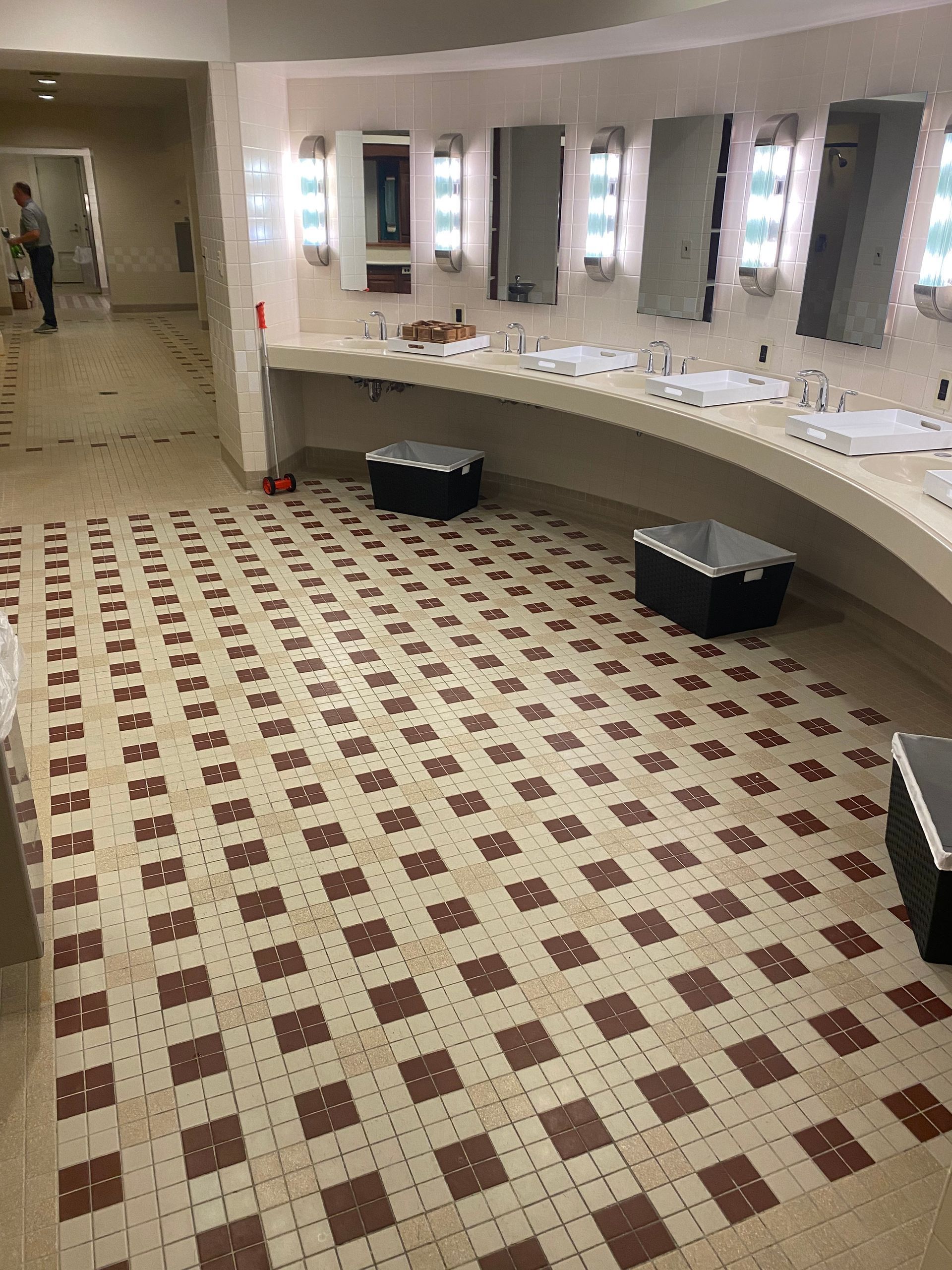 Public restroom with beige and maroon tiled floor, curved sink counter, and rectangular mirrors.