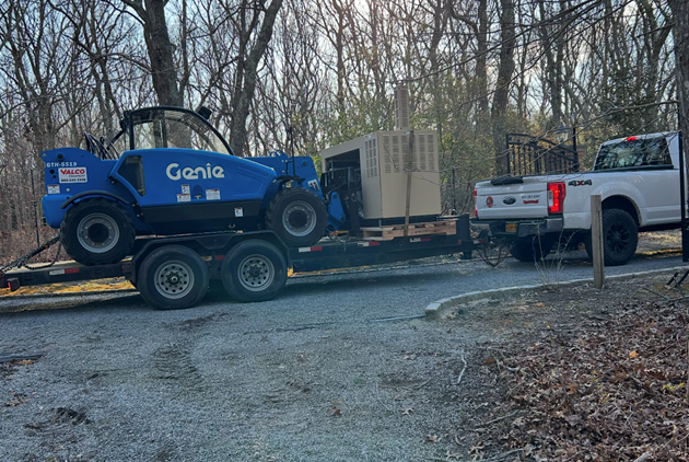 A truck is towing a forklift on a trailer.
