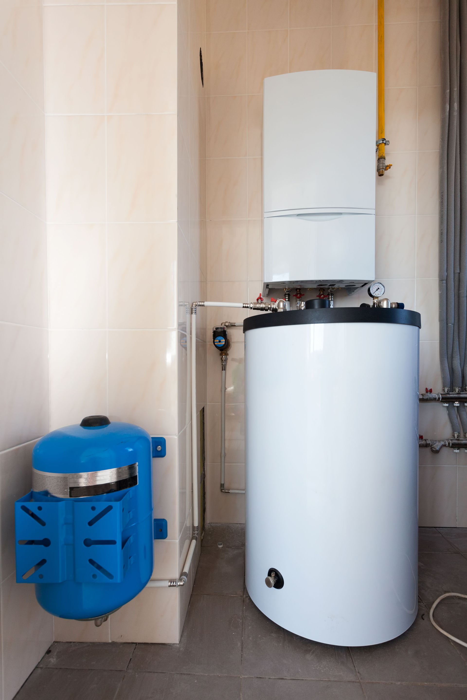 White water heater and blue expansion tank in a beige tiled utility room.