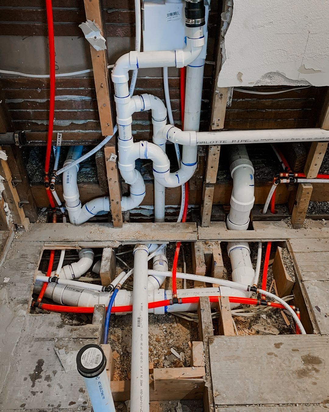 Open wall with exposed plumbing pipes, red and blue lines, and a floor cutout showing pipes below.
