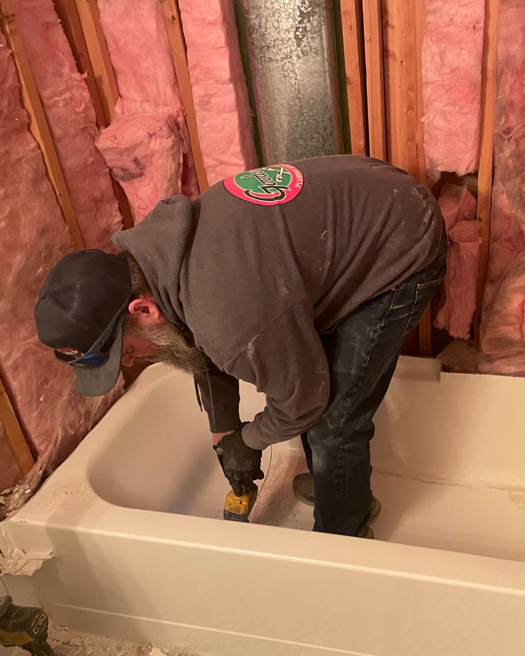 Worker installing a white bathtub in an unfinished bathroom with exposed pink insulation.
