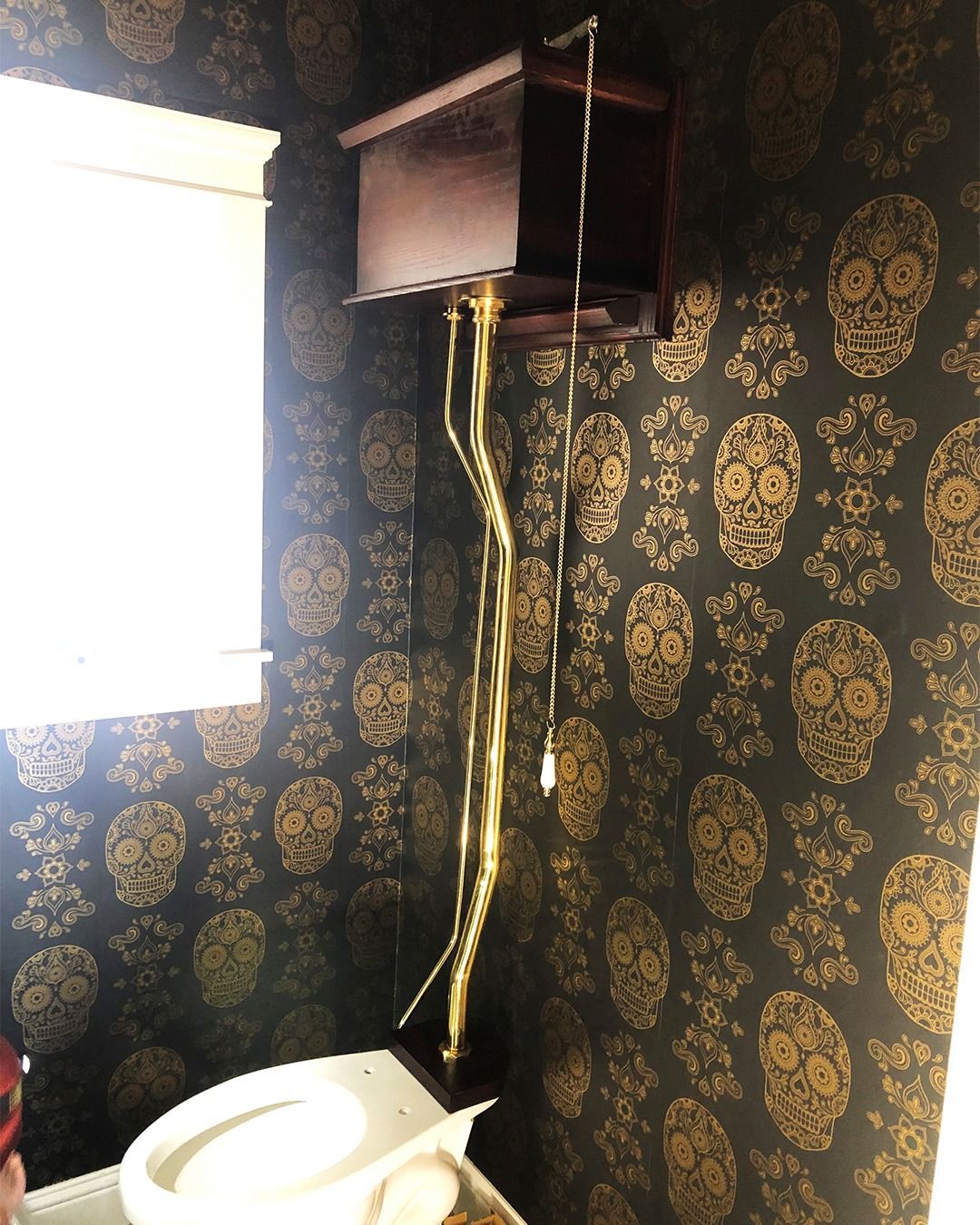 Wall-mounted black box with dangling cables above a toilet in a small bathroom with dark patterned wallpaper.