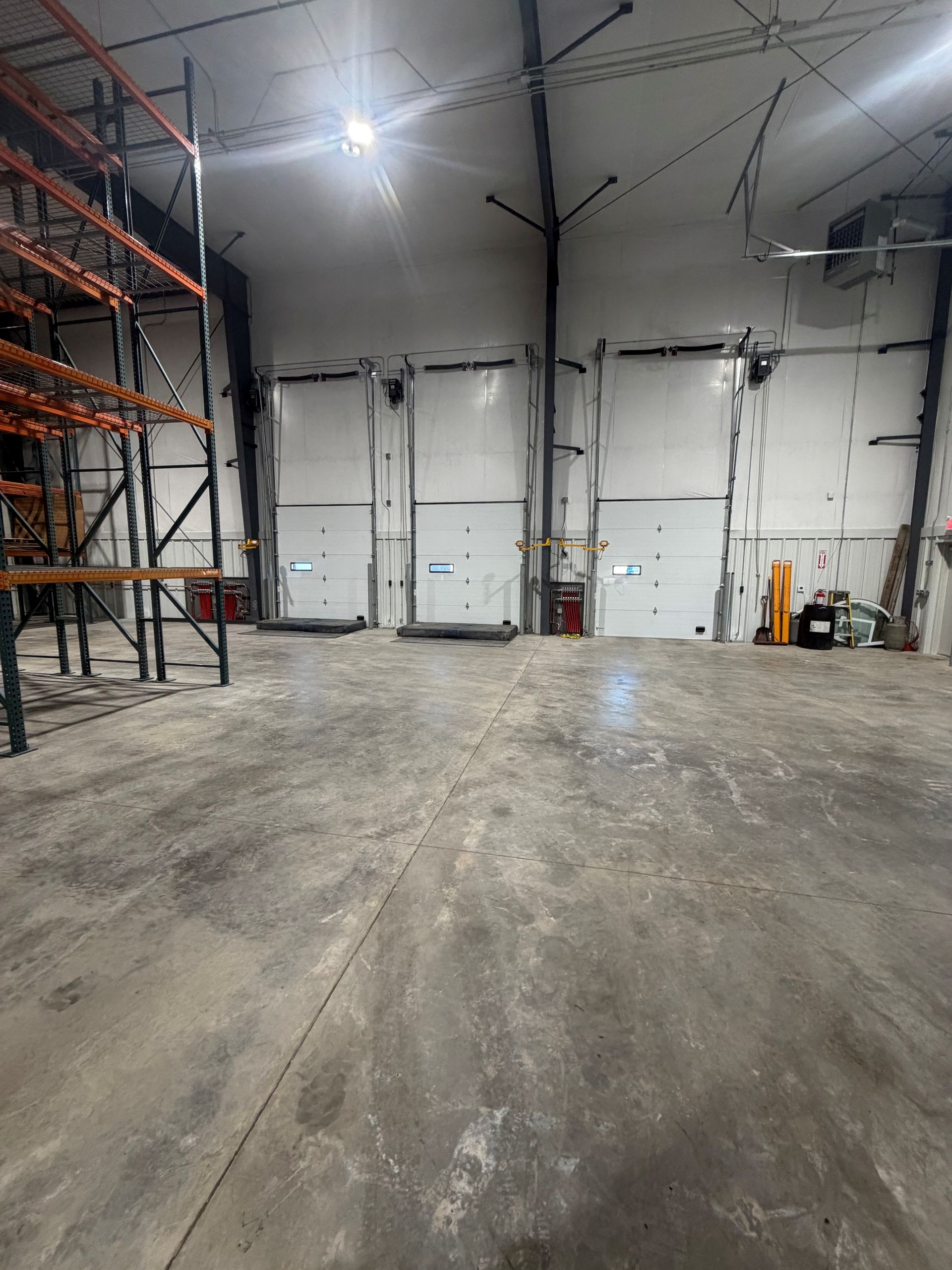 Empty warehouse interior with three loading dock doors and a concrete floor.