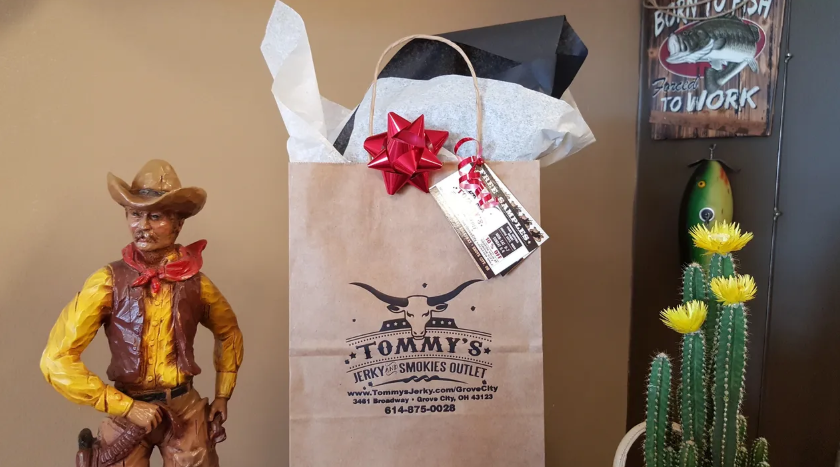Gift bag from Tommy's restaurant with bow, cowboy statue, and cactus next to a wall with decor.