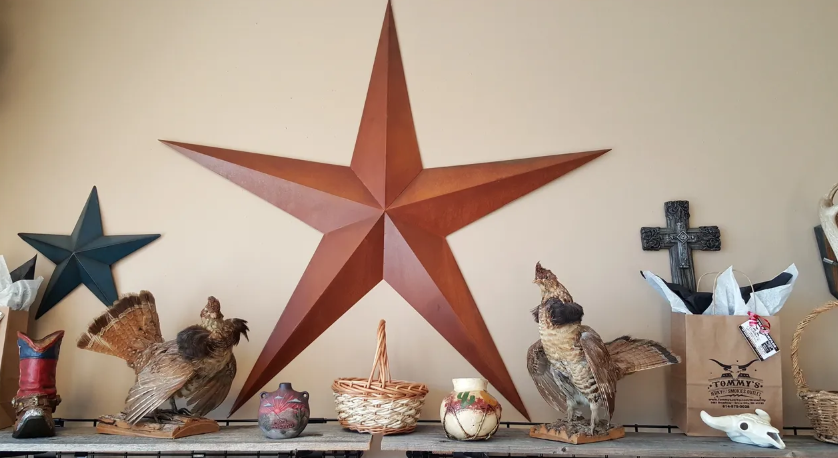 Shelf with large star, taxidermy birds, basket, pottery, and cross against a tan wall.
