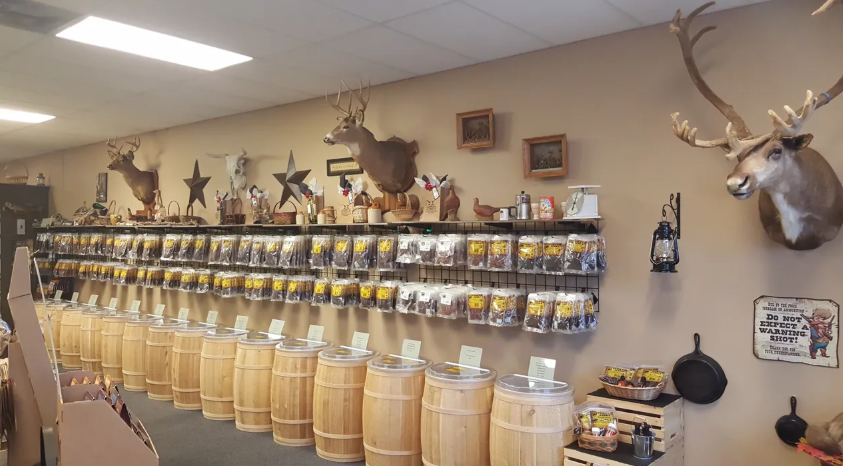 A store interior displays taxidermy, barrels, and various packaged goods along a beige wall.