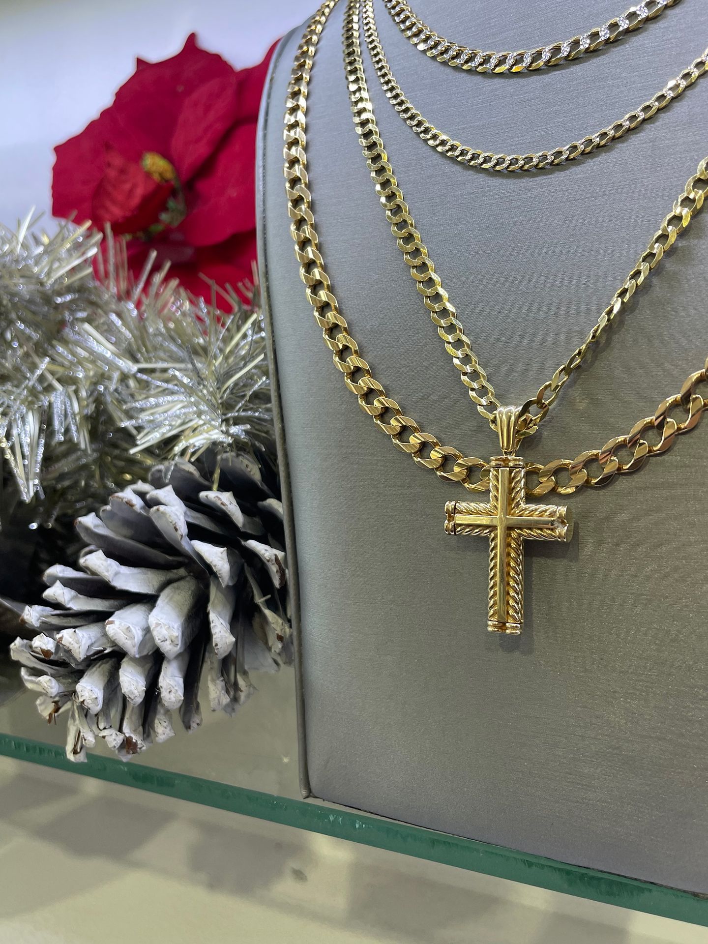 Gold necklaces with a cross pendant displayed on a gray background, with holiday decorations