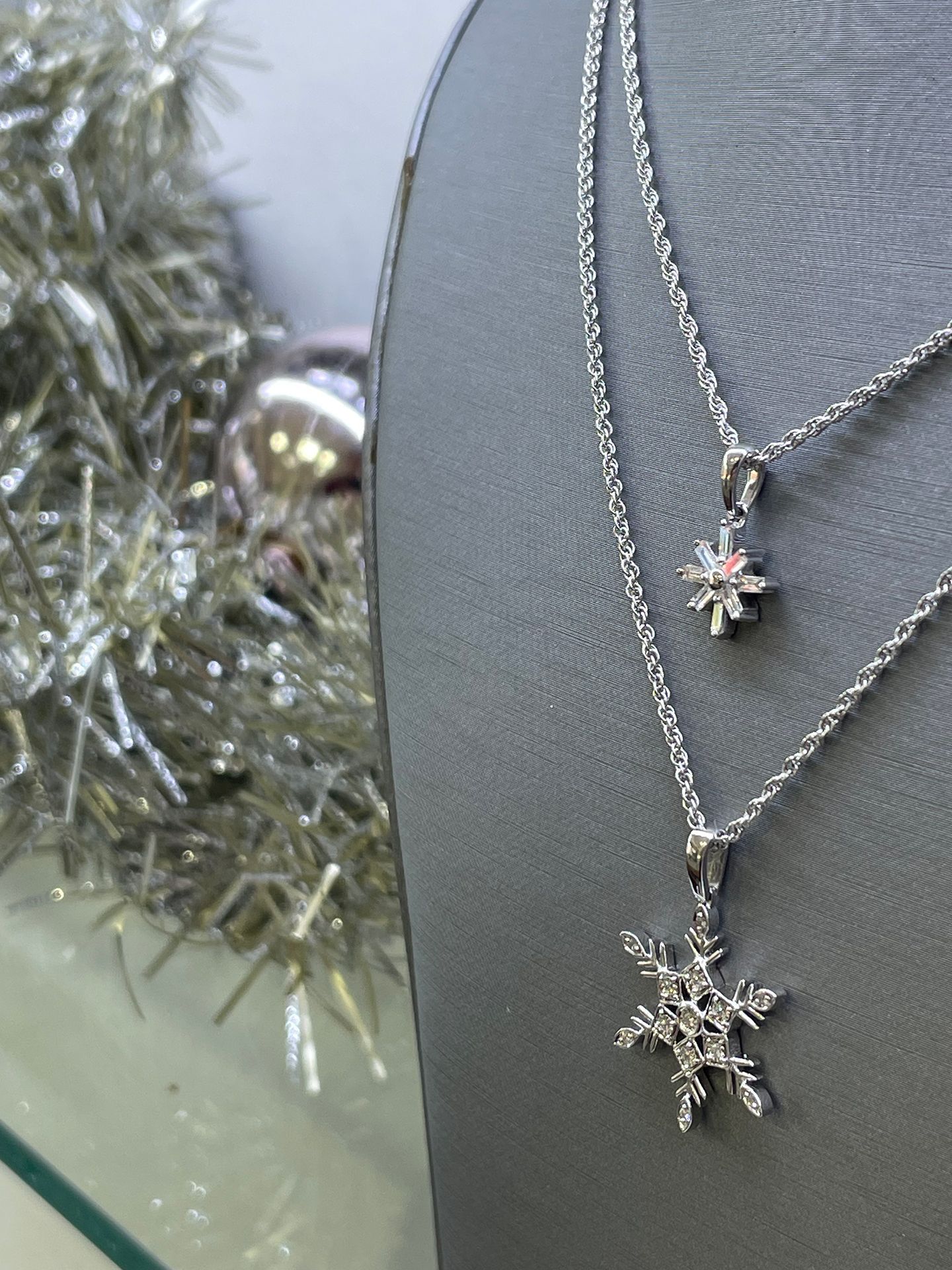 Two silver snowflake necklaces on a gray display stand