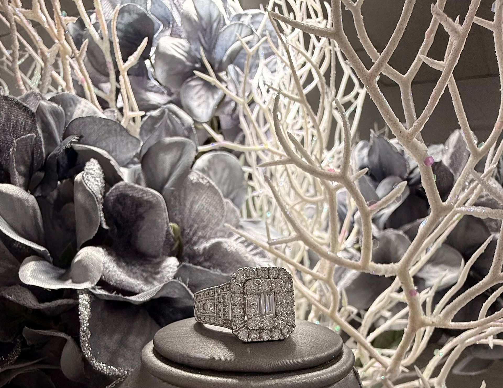 Diamond ring on a pedestal, with silver flowers and white branches in the background