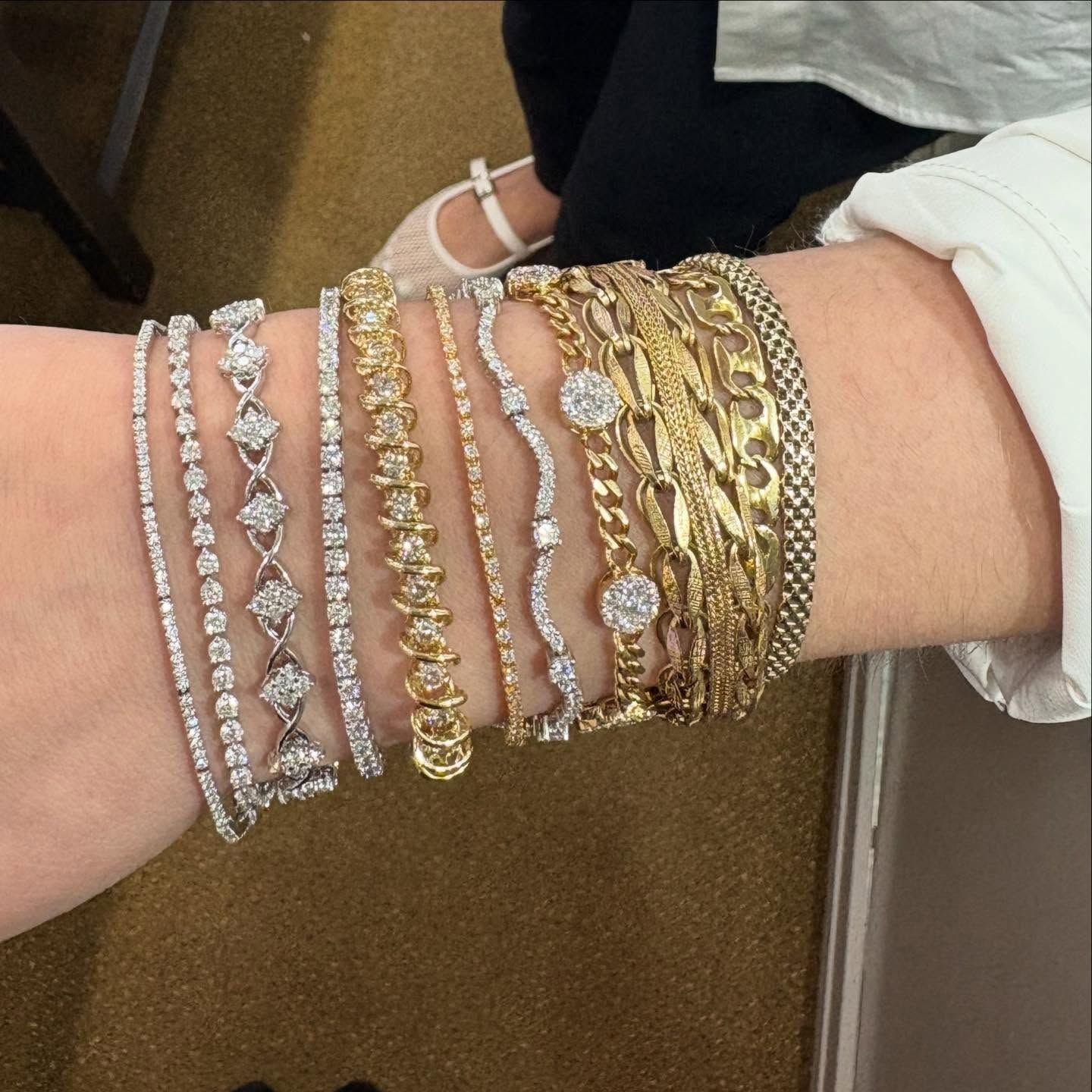 Wrist adorned with numerous gold and silver bracelets; person wearing a white shirt and black pants.