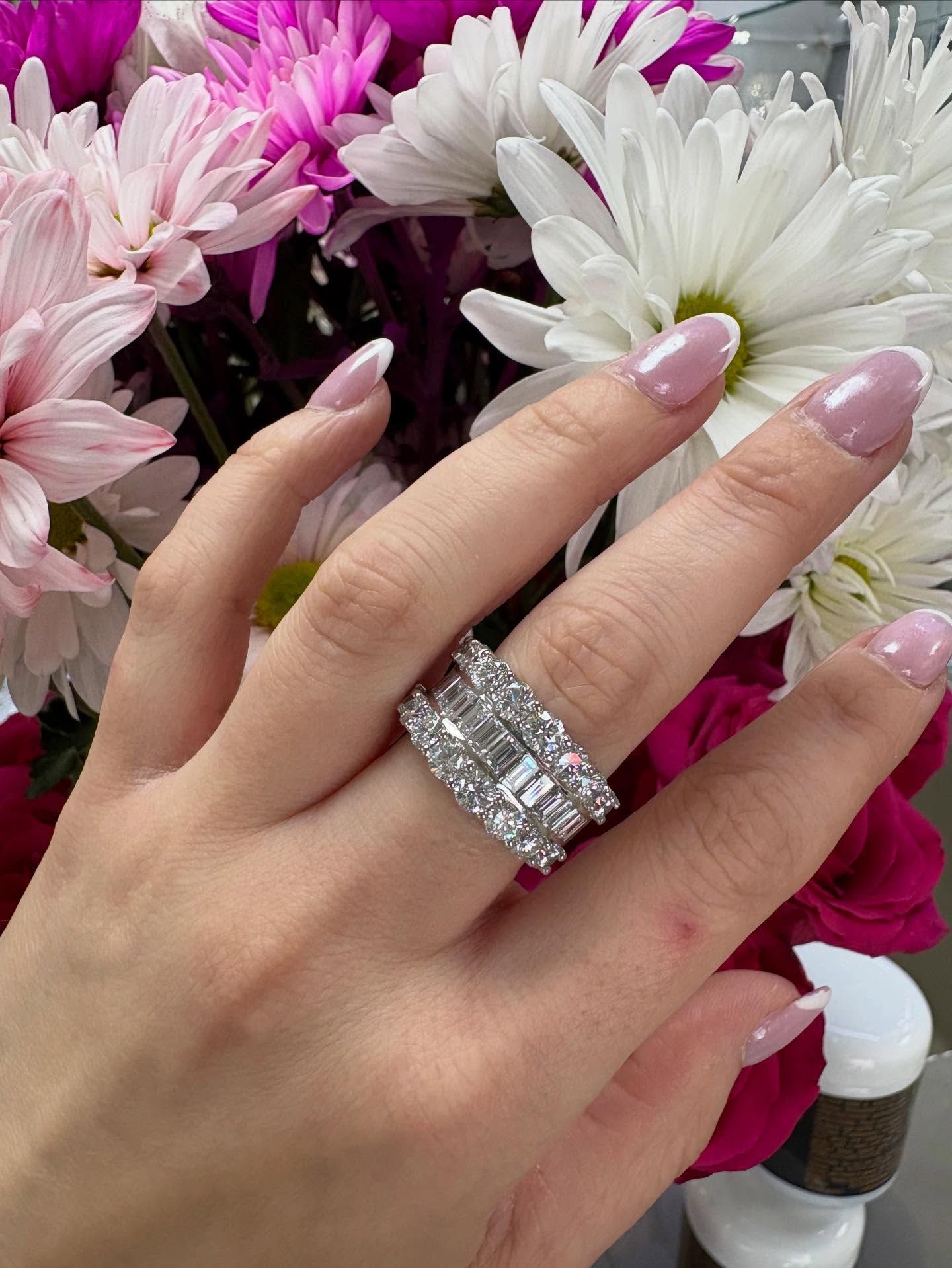 Hand with a large diamond ring on a flower background, with pink and white petals and long manicured nails.