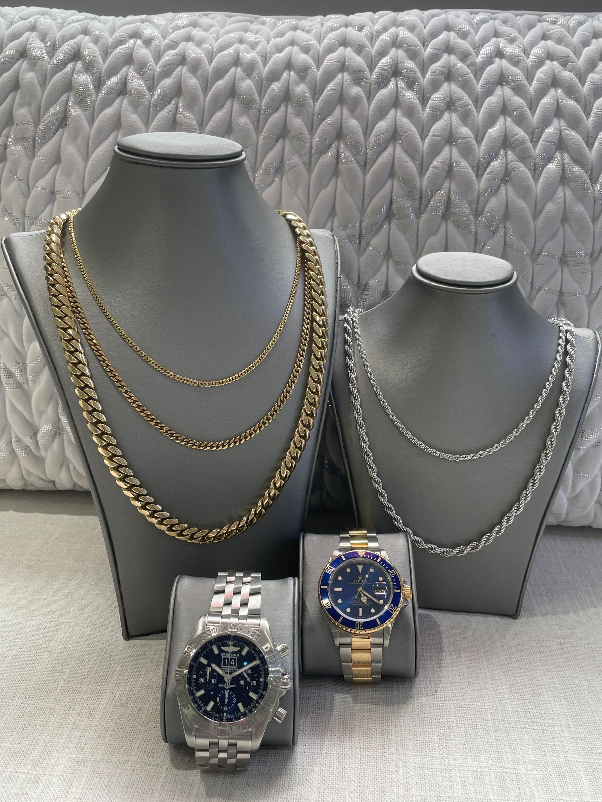 Three necklace display busts with gold and silver chains and two wristwatches in front