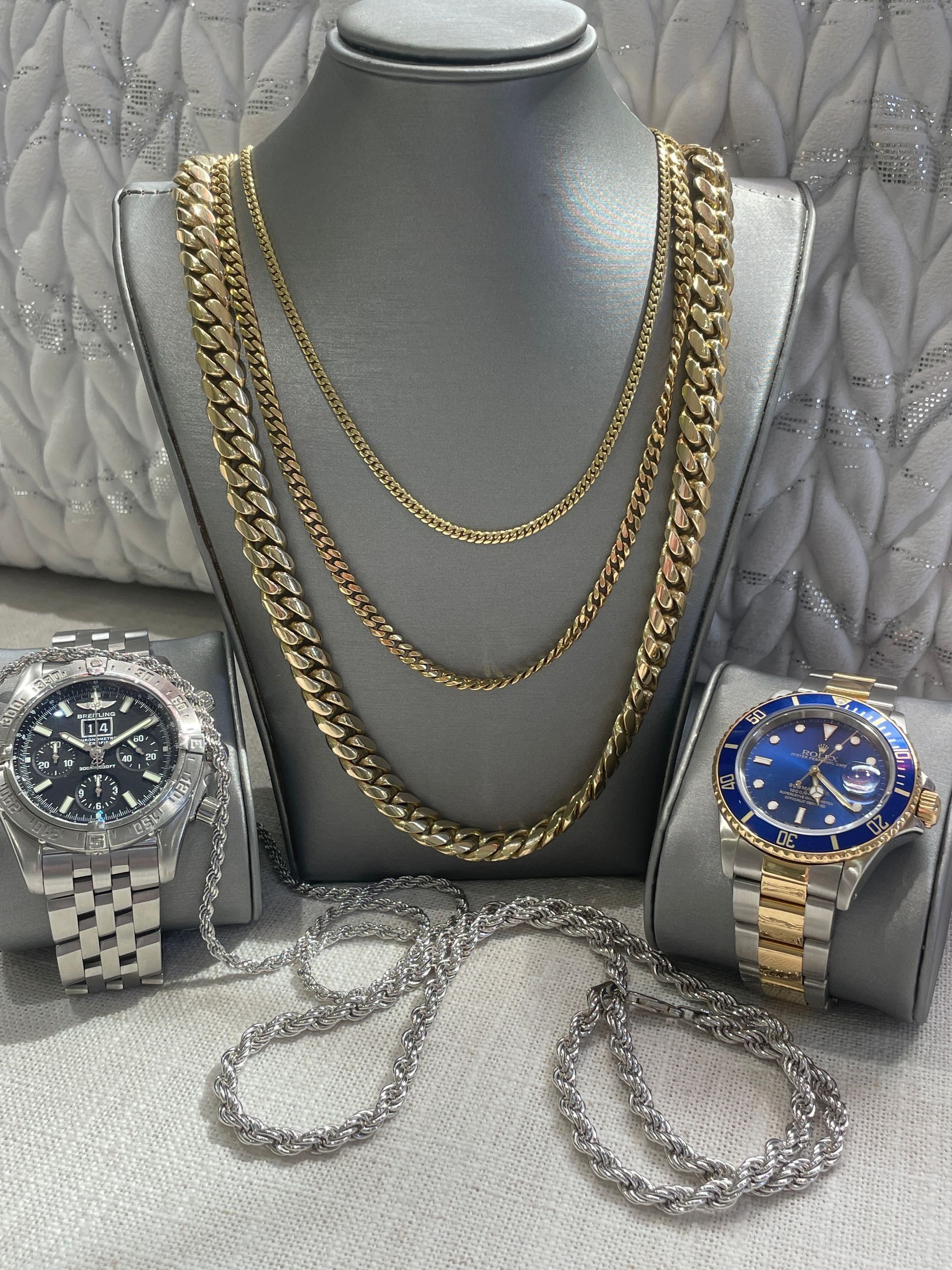 Gold necklaces and two wristwatches displayed on a gray jewelry bust