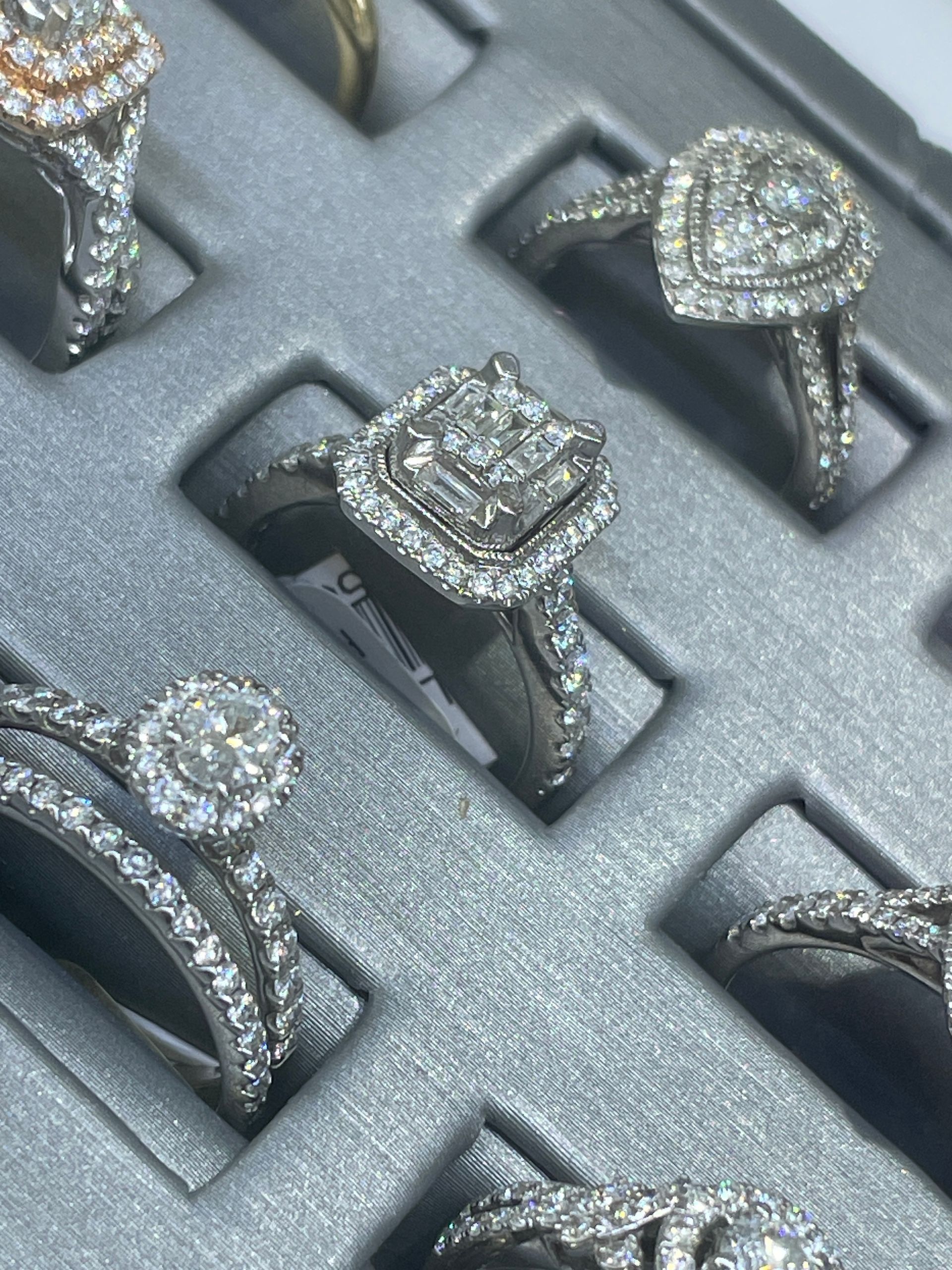 Assorted diamond rings displayed in a gray jewelry case, including round and square settings