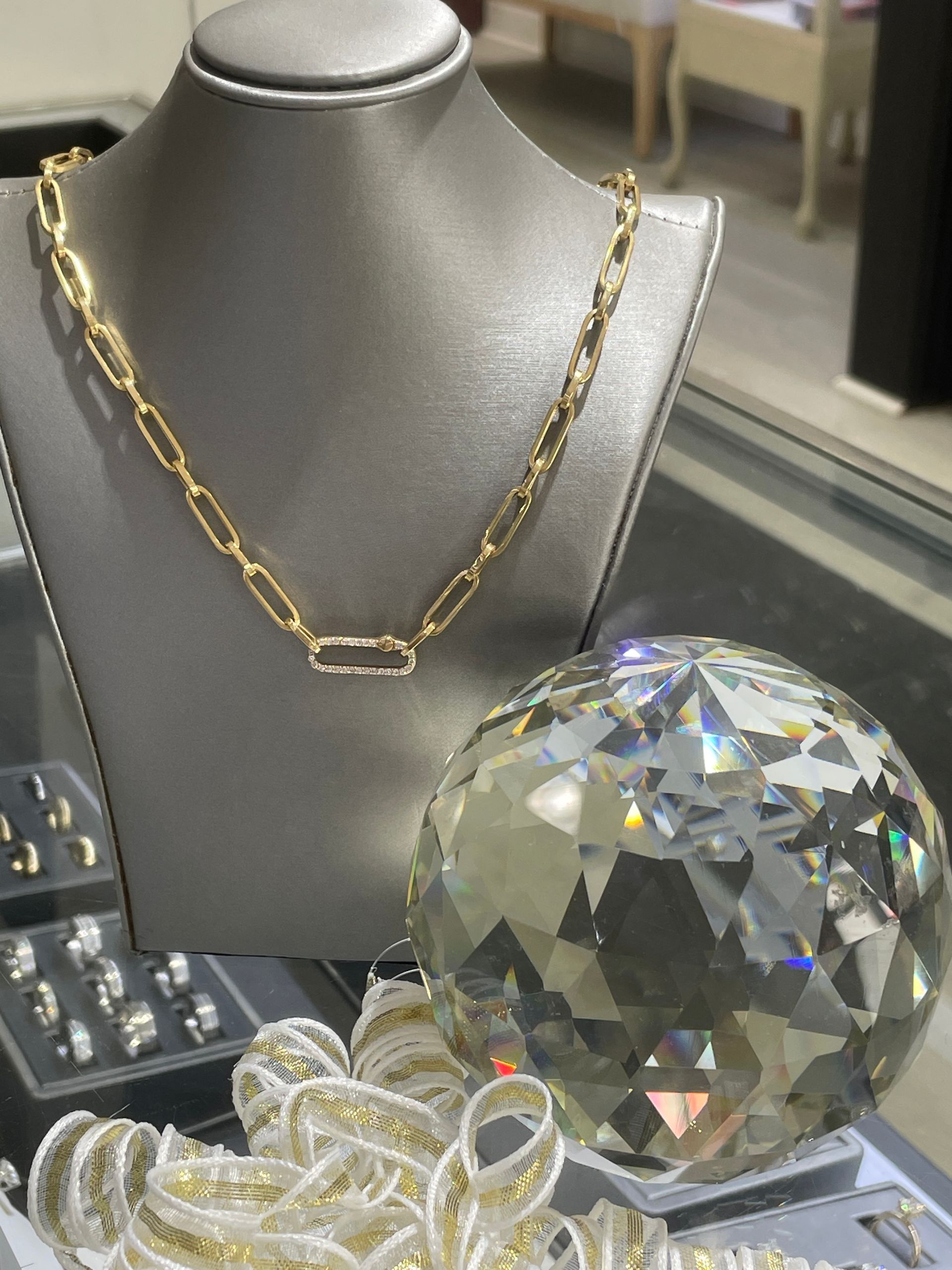 Gold chain necklace beside large faceted crystal sphere.