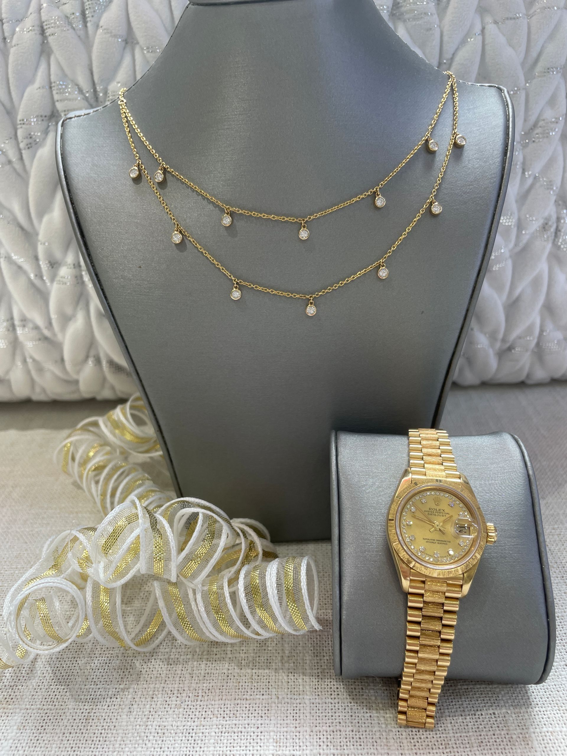 Gold jewelry display with layered necklaces, bracelet, and gold wristwatch on gray stands