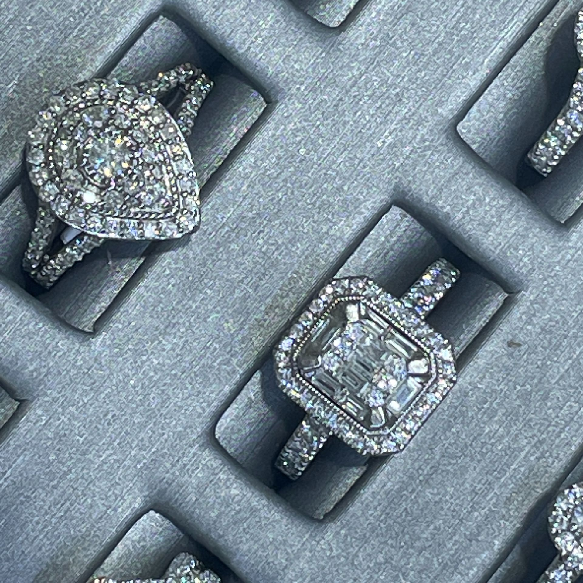 Diamond rings in a gray jewelry display case, including a pear-shaped and a square-cut ring