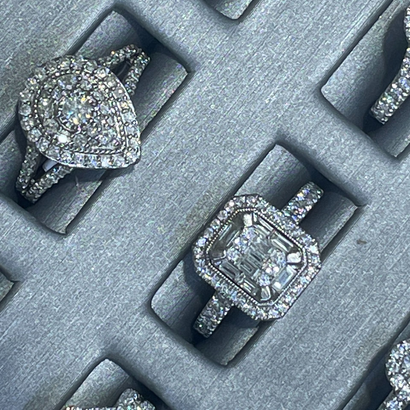 Diamond rings in a gray jewelry display case, including a pear-shaped and a square-cut ring