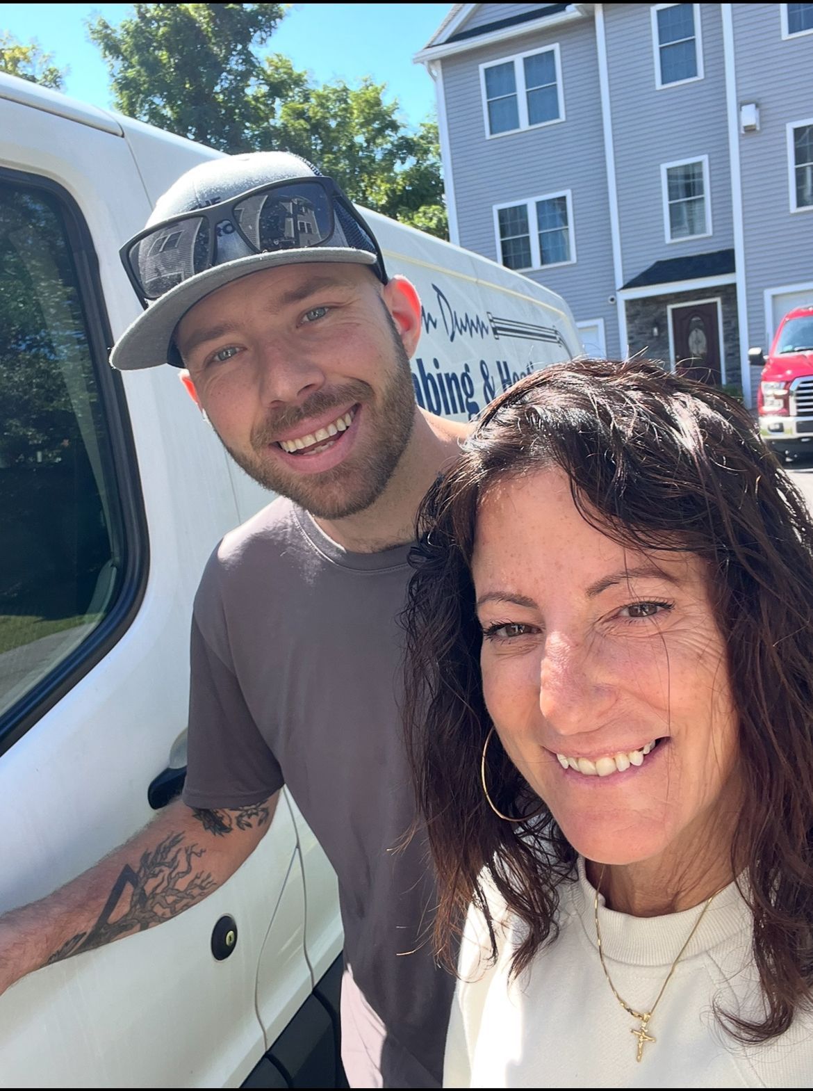Smiling man and woman next to a white van with business logo in front of a blue building.