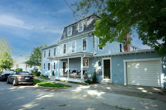 Blue two-story house with white porch and attached garage on a tree-lined street