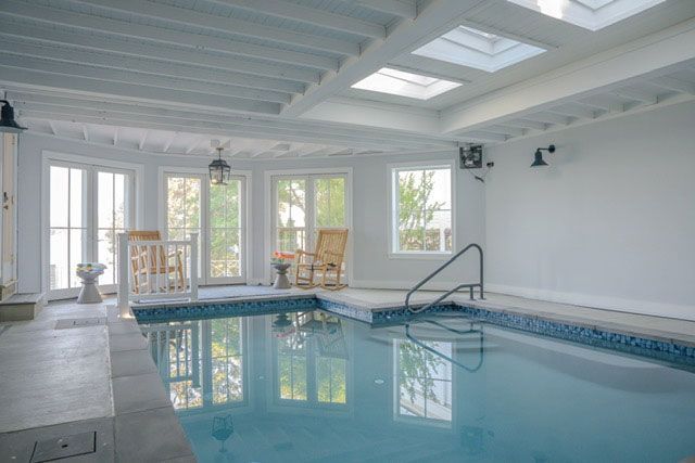 Indoor swimming pool room with skylights, white walls, and large windows overlooking a patio.