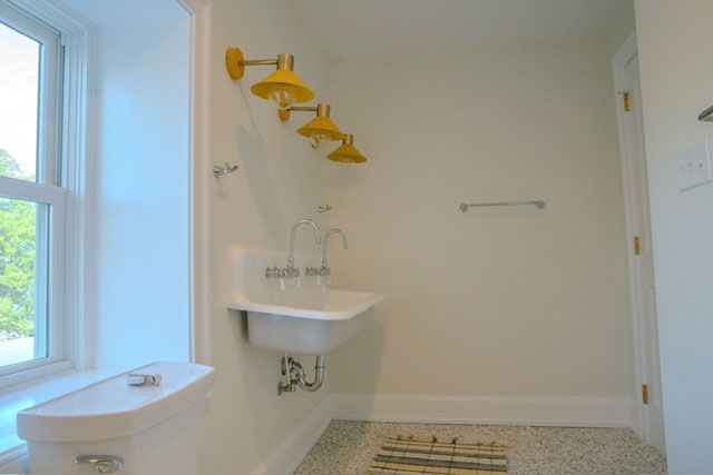 Bathroom with white walls, yellow towel racks, a sink, toilet, and window.