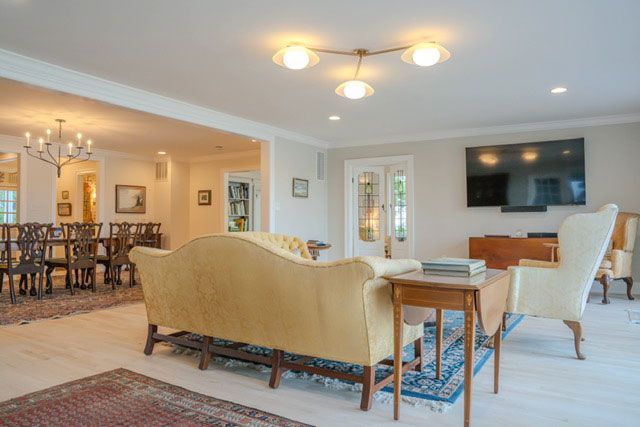 Bright open living room with beige sofas, dining area, and wall-mounted TV on a white wall