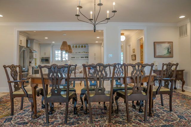 Elegant dining room with a long wooden table, ornate chairs, patterned rug, and kitchen pass-throughs
