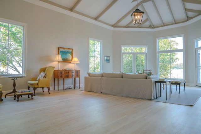 Bright living room with large windows, beige sofa, yellow chairs, and vaulted ceiling