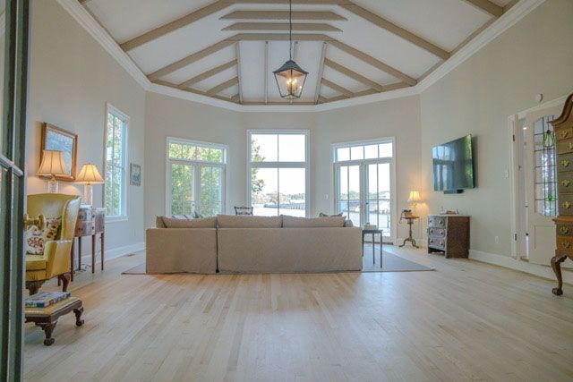 Bright living room with vaulted ceiling, beige sofa, large windows, and light wood floors.