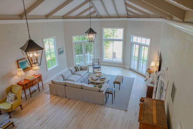 Bright living room with vaulted ceiling, large windows, and a beige sectional around a coffee table