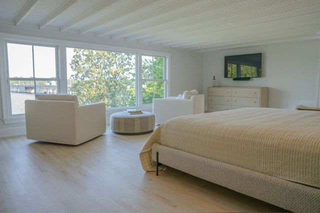 Bright minimalist bedroom with a large bed, two chairs, a dresser, and floor-to-ceiling windows.